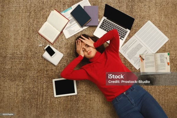 An exhausted student, who lies on the floor, appears overwhelmed due to studying for her exams. (Credit: Unsplashed.com)